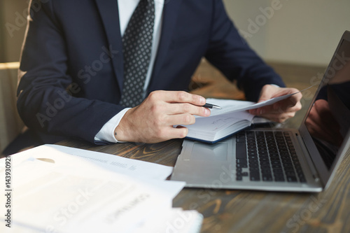 Closeup portrait of unrecognizable successful businessman analyzing contract documents at desk with laptop