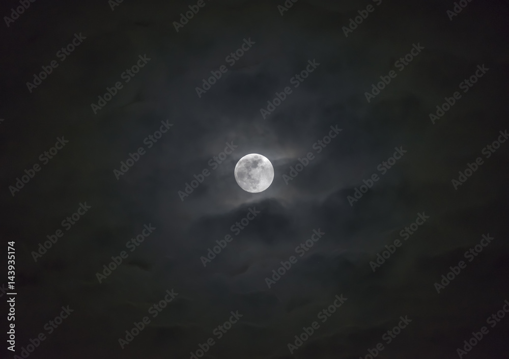 Glowing full moon behind wispy layers of moody clouds, atmospheric night sky scene