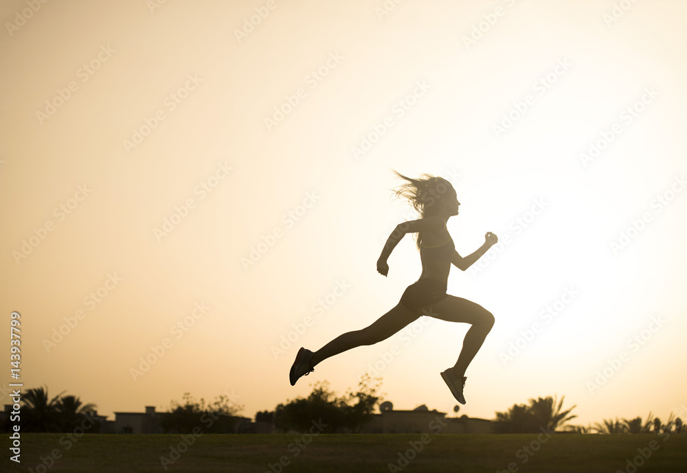 Dark silhouette of an athletic woman leaping as she jogs with a sunset in the background  