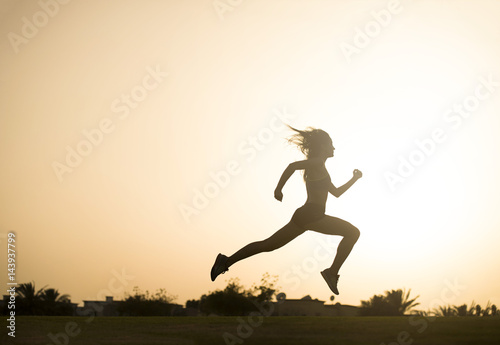 Dark silhouette of an athletic woman leaping as she jogs with a sunset in the background 