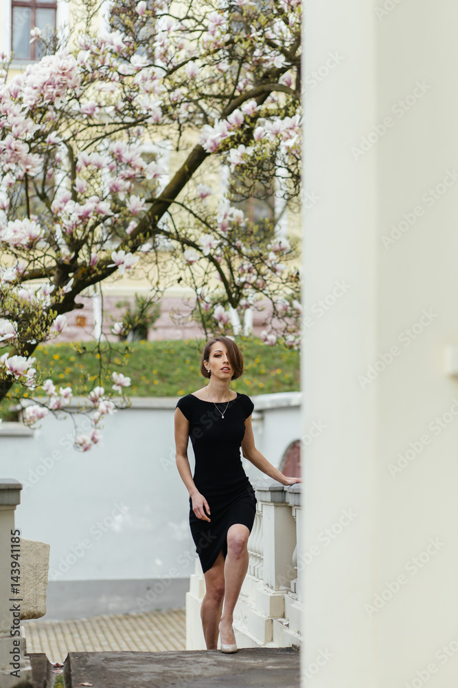 Beautiful healthy young woman in black dress with magnolia flowers Beautiful healthy young woman in black dress with magnolia flowers