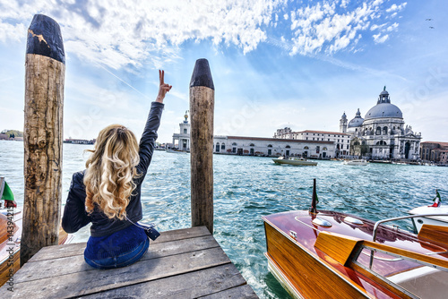 Tableau sur toile Blonde girl sitting on the pier in Venice. Back view
