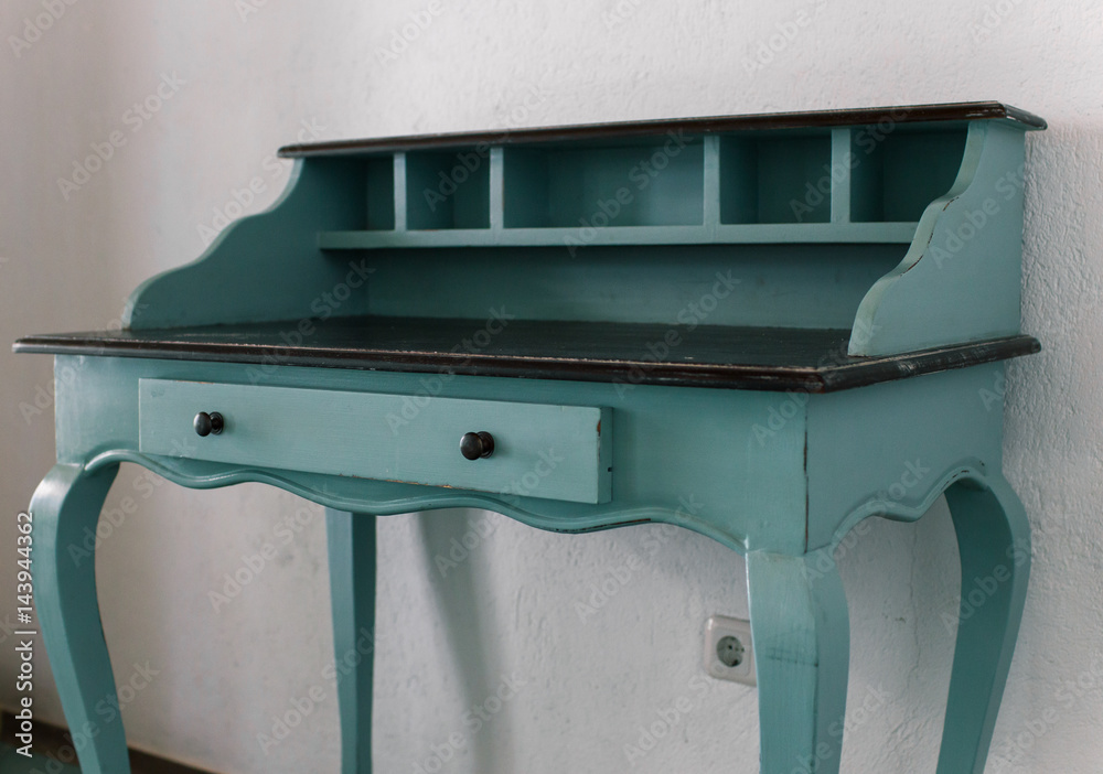 Blue vintage table of drawers stands near white wall