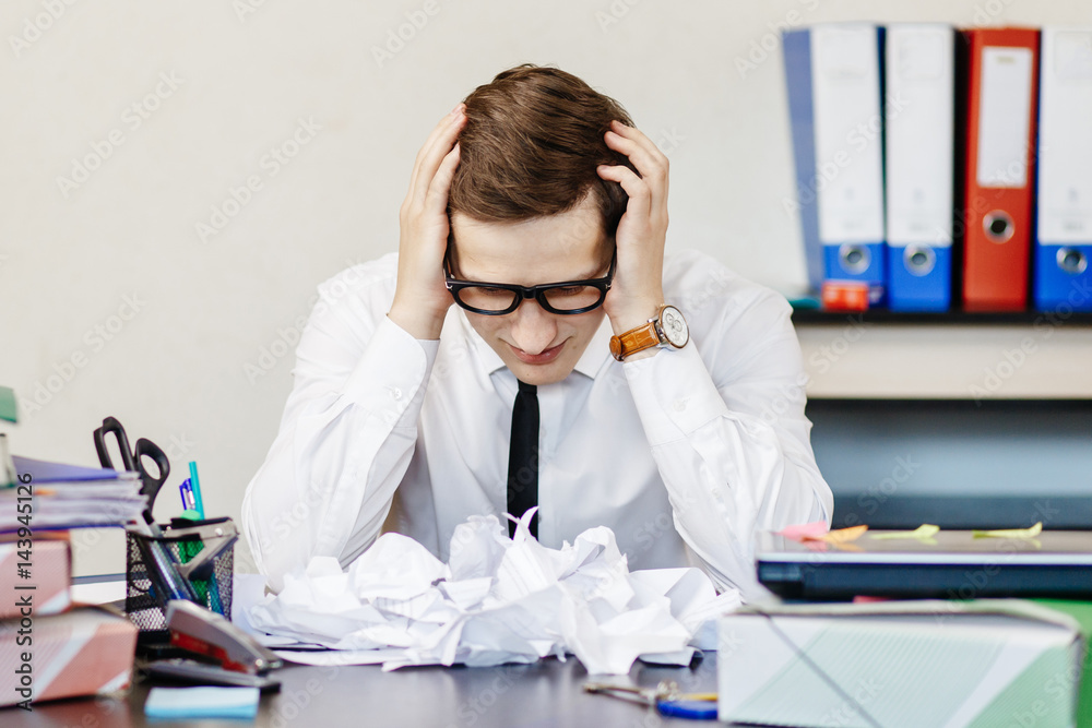 Young businessman sitting at his workplace in the office and looking at torn sheets of paper Young businessman sitting at his workplace in the office and looking at torn sheets of paper