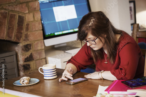 A young woman sitting with a cup of coffee and scrolling through her messages on her smart phone.