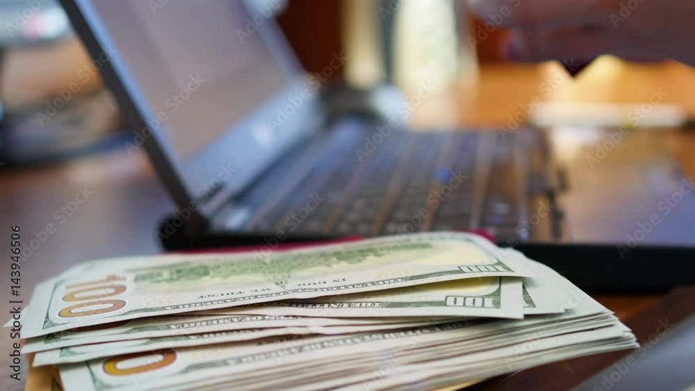 Hands typing text on laptop, close-up of money and passports Hands typing text on laptop, close-up of money and passports