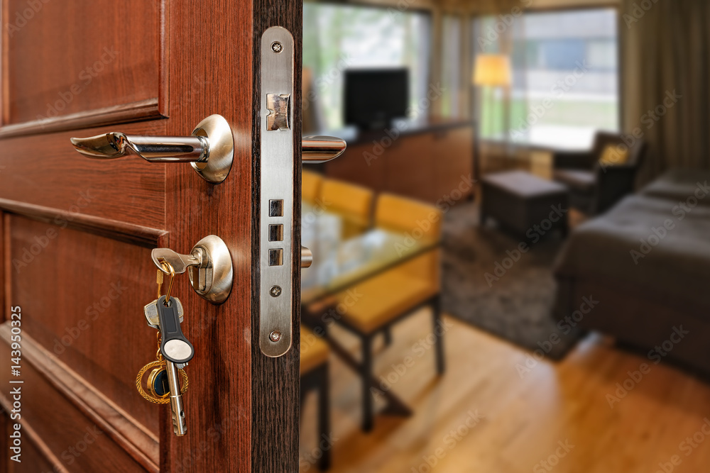 Naklejka premium Slightly opened wooden door with group of modern keys on keychain as a concept for home ownership or for security and door policy privacy