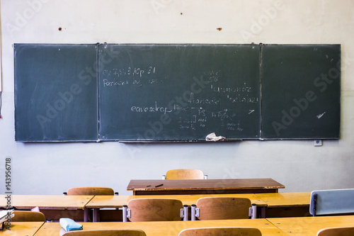 Classroom with empty wooden desks and with green board
