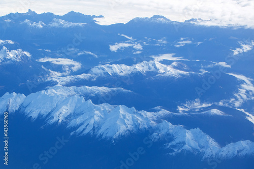 Idyllic snowy mountain peaks under clouds from plane © Volodymyr