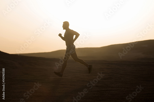 Man runner running in dune at sunset
