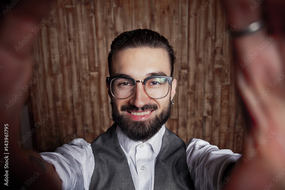 Fototapeta premium Funny stylish young guy doing selfie on a wooden background