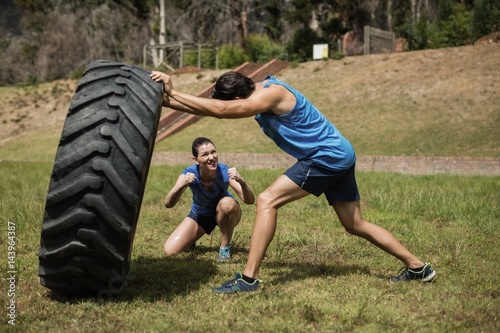Fit man flipping a tire while trainer cheering 