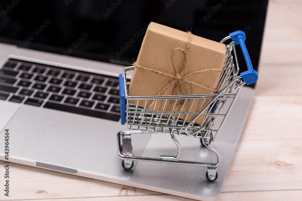Shopping time. A laptop and shopping cart gift box wrapped with paper kraft on table.