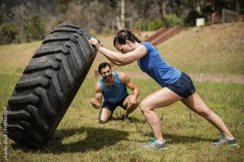Fit woman flipping a tire while trainer cheering 