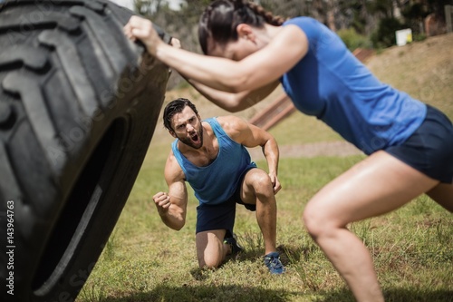 Fit woman flipping a tire while trainer cheering 