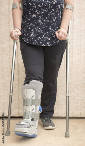 Unrecognisable woman wearing a medical orthopaedic boot with cruches photo