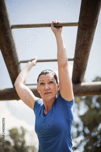 Fit woman climbing horizontal bars during obstacle course
