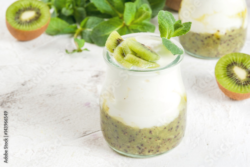 Fresh homemade organic Greek yogurt with kiwi puree, pieces of kiwi and mint. On a white stone table, with mint leaves and full and half of fruits. Copy space