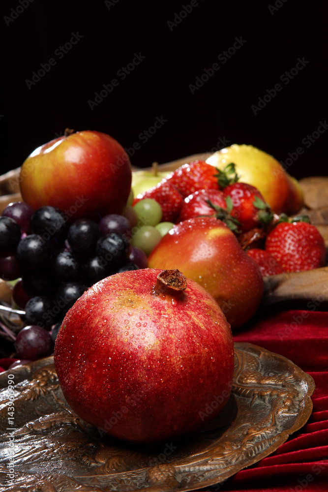 Ripe pomegranate in droplets of water on an old dish against a background of many fruits, copyspace Ripe pomegranate in droplets of water on an old dish against a background of many fruits, copyspace