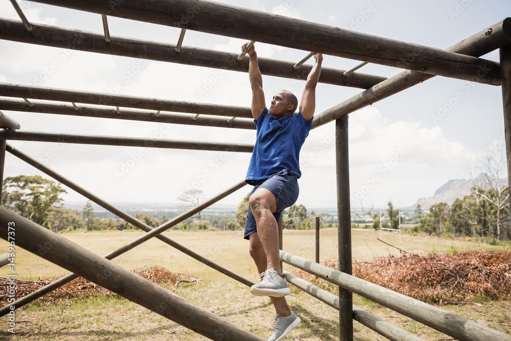 Fit man climbing horizontal bars during obstacle course