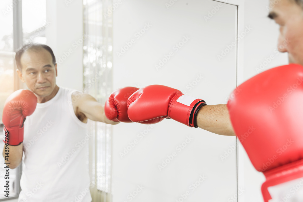 Portrait of Asian senior fighter man punching with red boxing gloves. Boxing practicing.