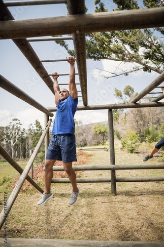 Fit man climbing horizontal bars during obstacle course
