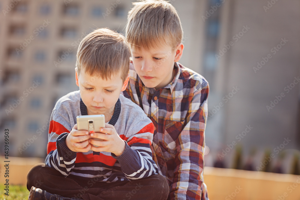 Children with mobile phone outdoor. Boys smiling, looking to phone, playing  games or using application Stock Photo