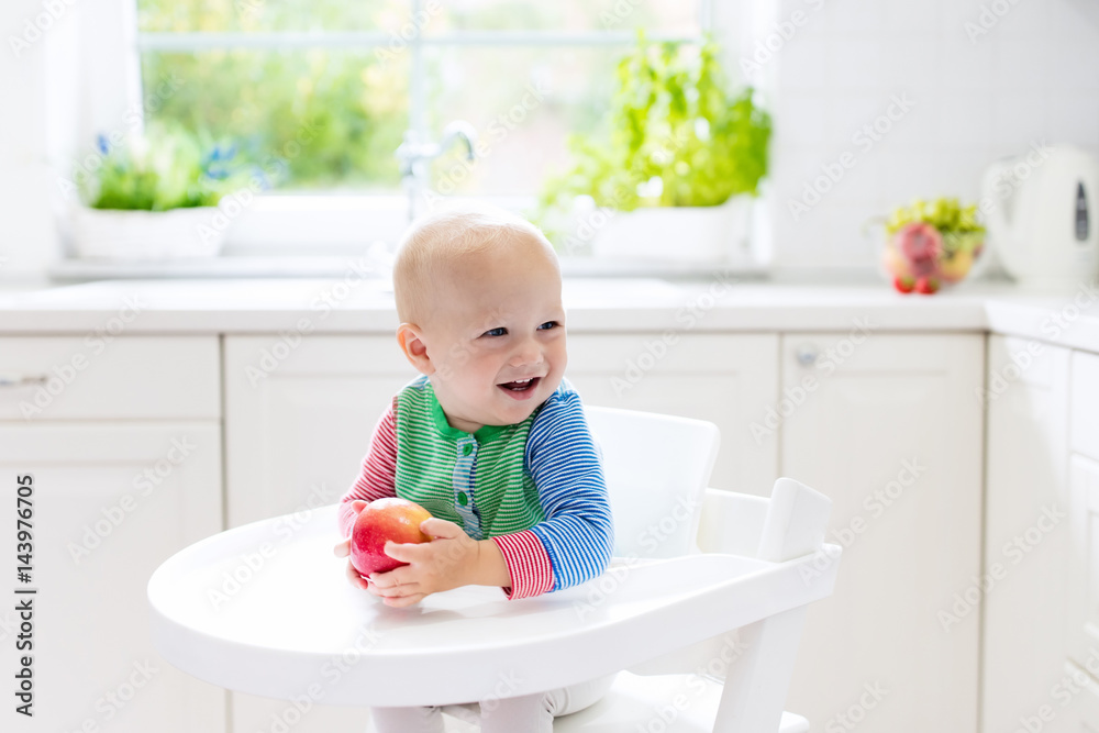 Baby boy eating apple in white kitchen at home Baby boy eating apple in white kitchen at home