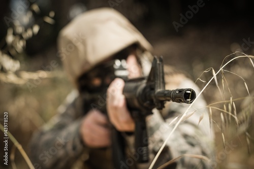 Military soldier hiding in grass while guarding with a rifle