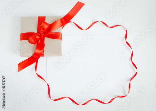 Holiday Post card. Beige gift box with red ribbon and a sheet of paper. Copy space White stone background 
