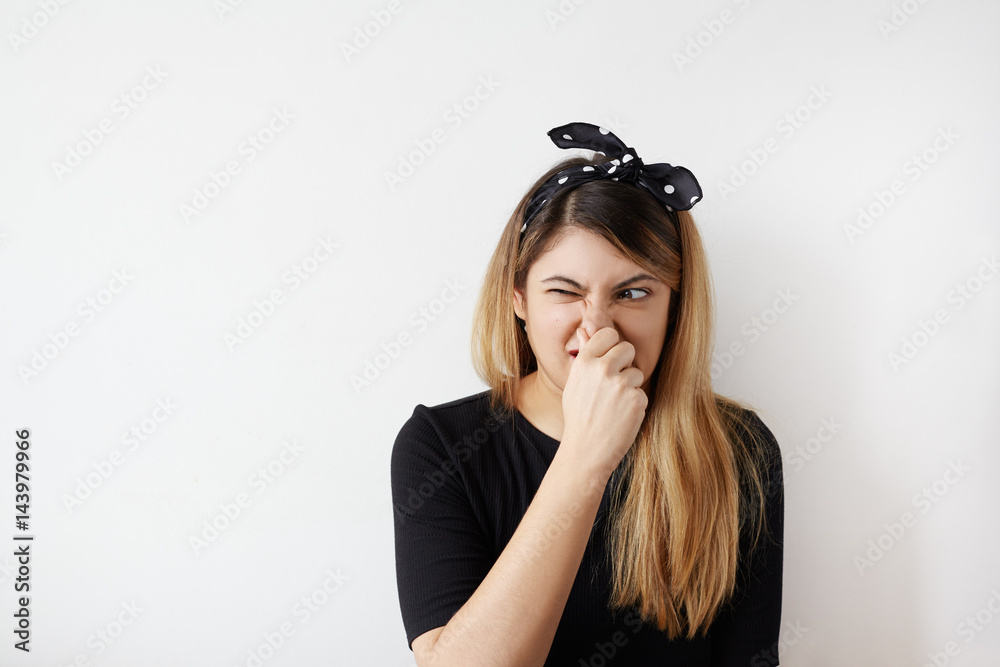 Female gesture smells bad. Portrait of woman wearing casually pinches nose with fingers hands looks with disgust something stinks bad smell situation. Human face expression body language reaction - obrazy, fototapety, plakaty 