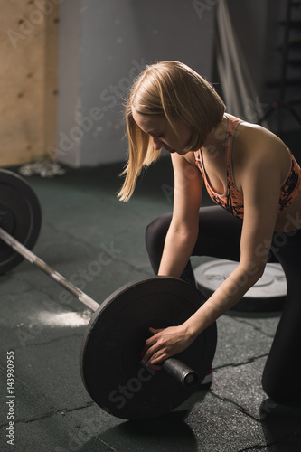 Fit power athletic confident young woman crossfit trainer doing exercises with heavy weight barbell plate in gym rising hand. Fitness muscular body, strong hand on dark background Pumping up muscles photo