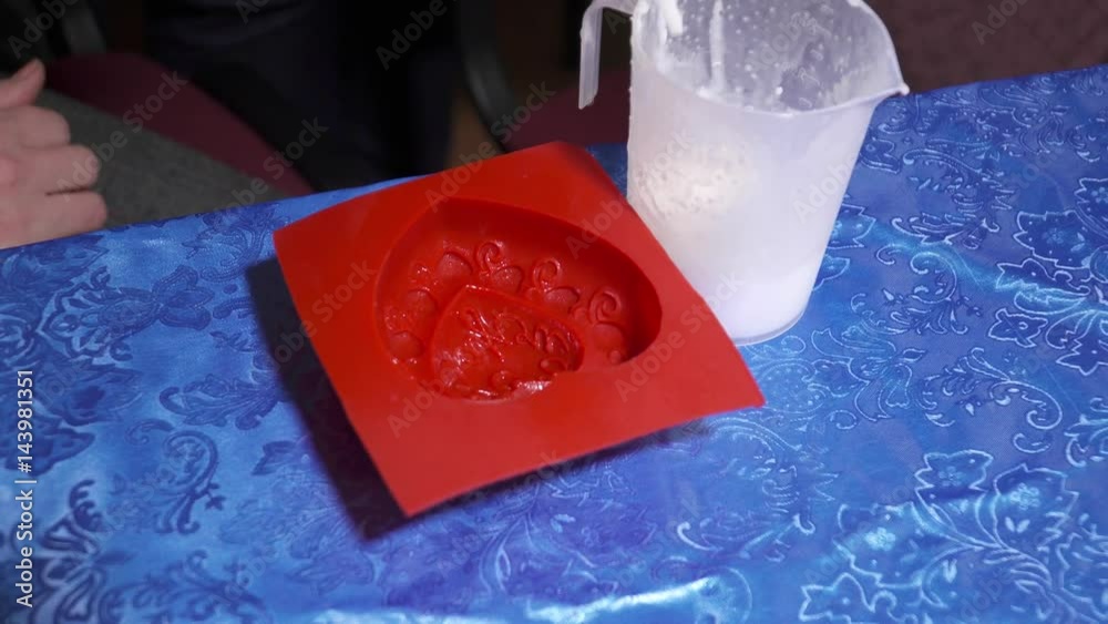 Woman's hands pouring soap base to the red template for handmade soap creation