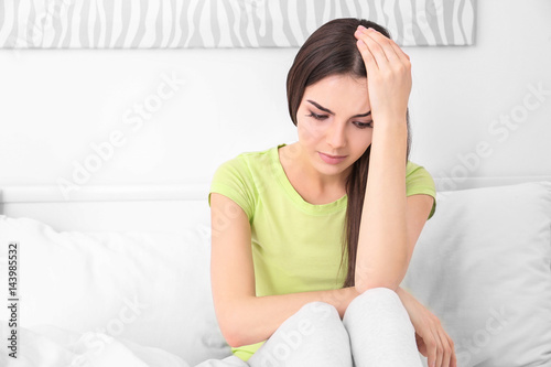 Young sick woman sitting on bed at home