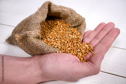 Closeup of young man's hand holding a sack with a buckwheat on white wooden table photo