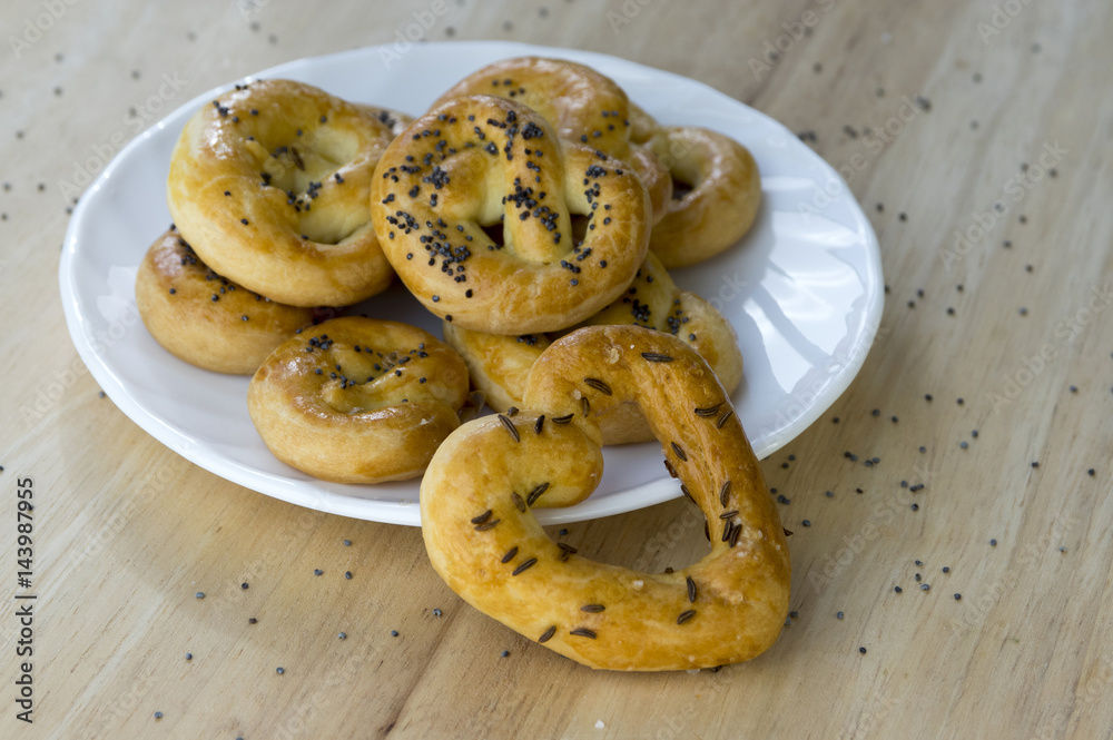 Baked fresh pretzels on white plate, heart and twisted knot shapes, covered with poppy seeds salt and caraway seeds Baked fresh pretzels on white plate, heart and twisted knot shapes, covered with poppy seeds salt and caraway seeds