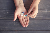 Hands of senior woman with pills on wooden background
