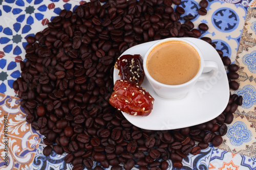 Cup of Arabian Coffee on an Oriental Colorful Background / Cup of Espresso on an Oriental Colorful Background with Flowers, Rings, and Tamr dates  photo