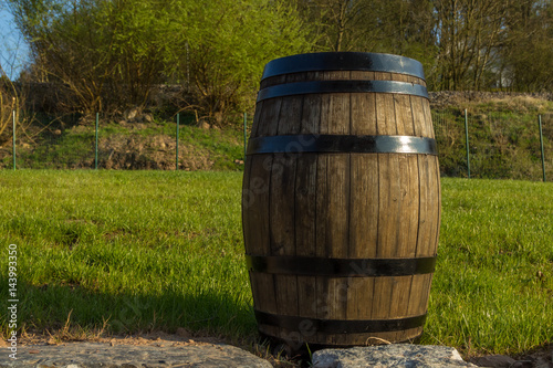 Oak vintage barrel on the right with green lawn, trees and stones as background
