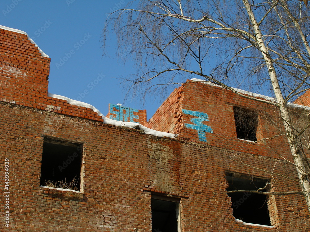 The fragment of the abandoned unfinished brick building with bodies of birches