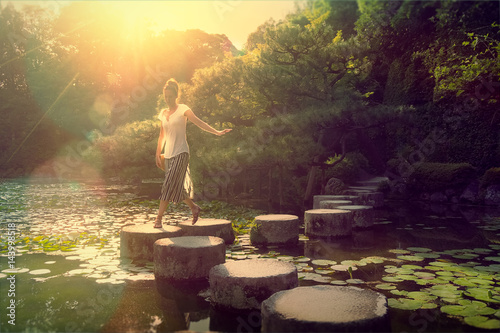 Young woman stepping on lake stone path in Kyoto Japan at sunset