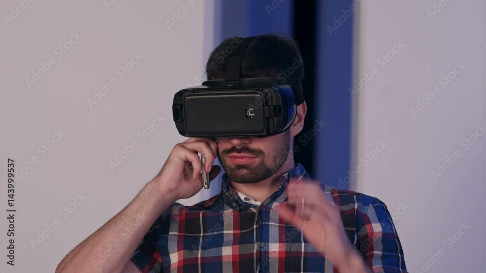 Serious young man in virtual reality glasses talking on the phone Serious young man in virtual reality glasses talking on the phone