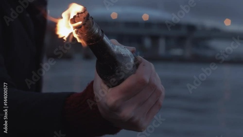 Hand of young man clutching burning Molotov cocktail bottlestanding on coast