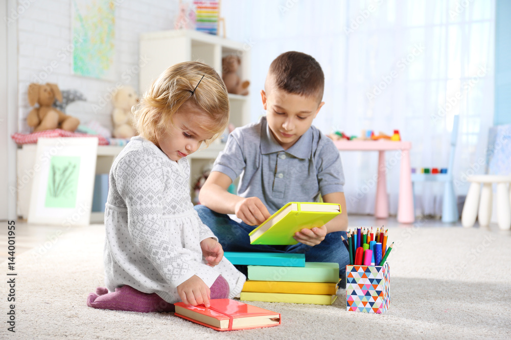 Cute little brother and sister sitting on floor with colorful notebooks