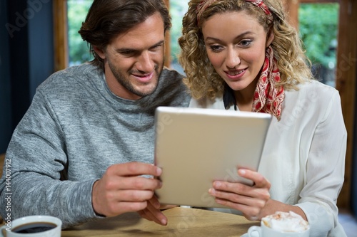 Loving couple using tablet computer at table in cafeteria