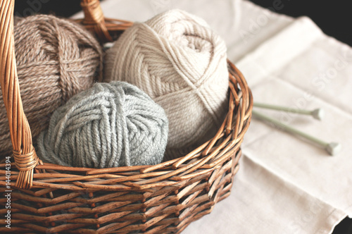 Wool yarn and knitting needles in basket on white napkin