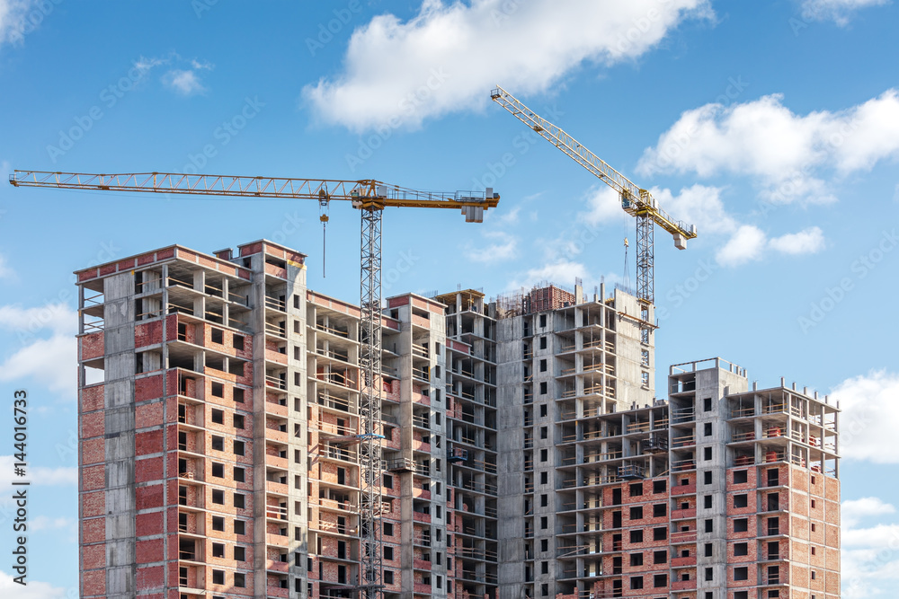 unfinished high-rise building and tower cranes on blue sky background unfinished high-rise building and tower cranes on blue sky background