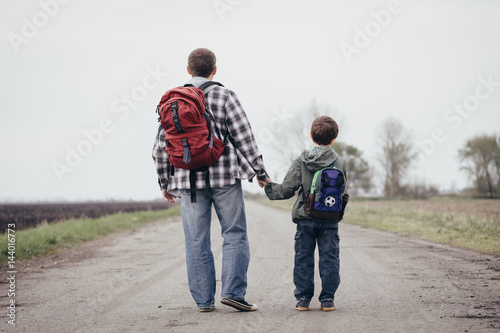 Father and son walking on the road at the day time.