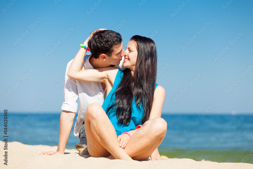 photo of cute couple sitting on the beach and kissing on the wonderful sea background