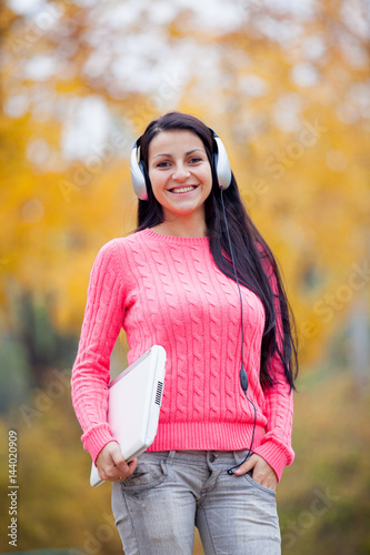 photo of beautiful young woman with laptop and headphones on the wonderful yellow trees background